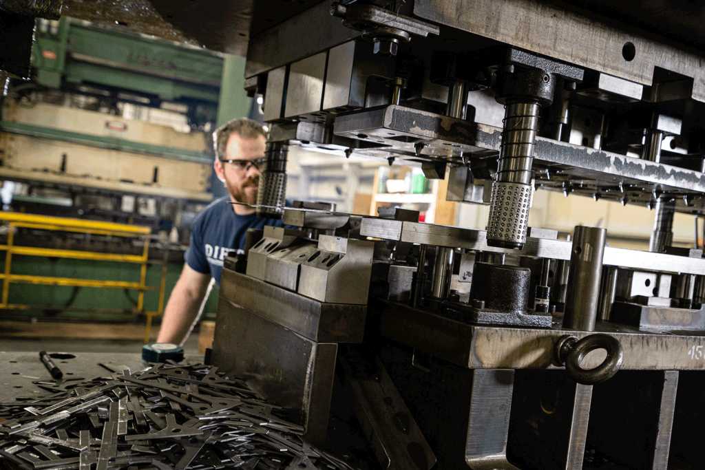 A man with goggle and a blue Dietech shirt operating a stamping machine.