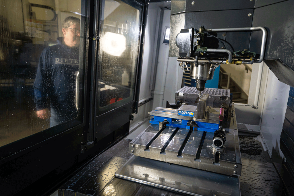 A man with goggle and a blue Dietech shirt operating a CNC machine.