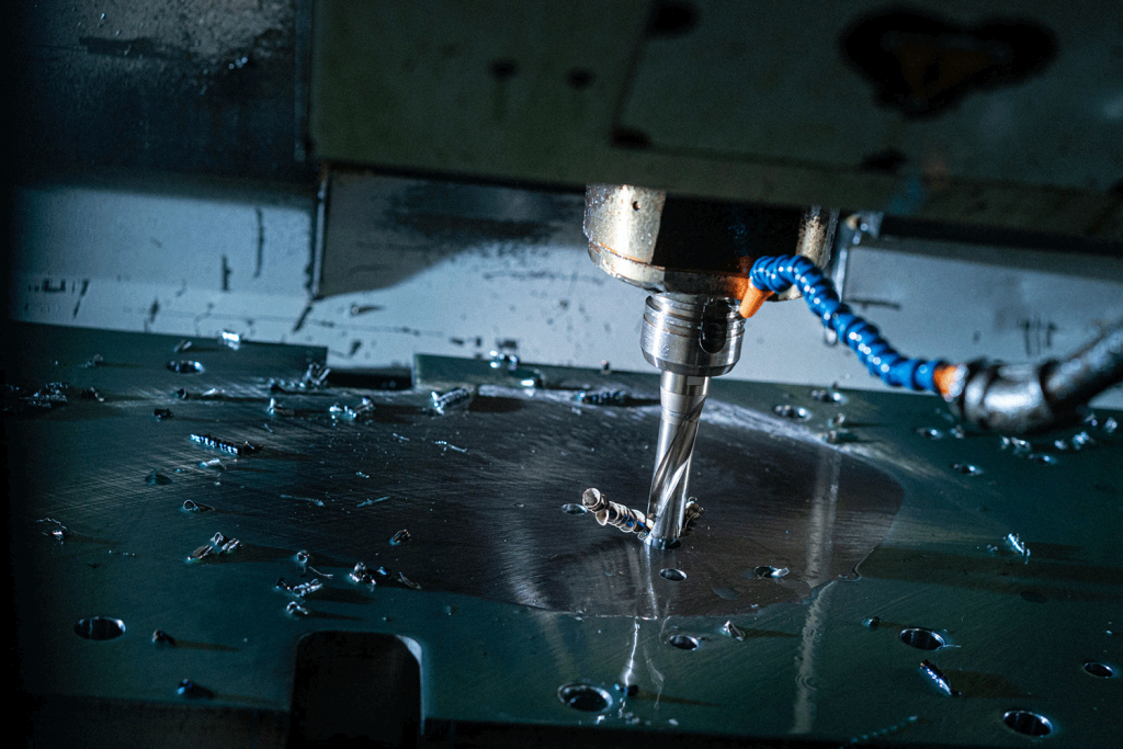 A water-cooled drill bores into steel turning up flakes of metal.