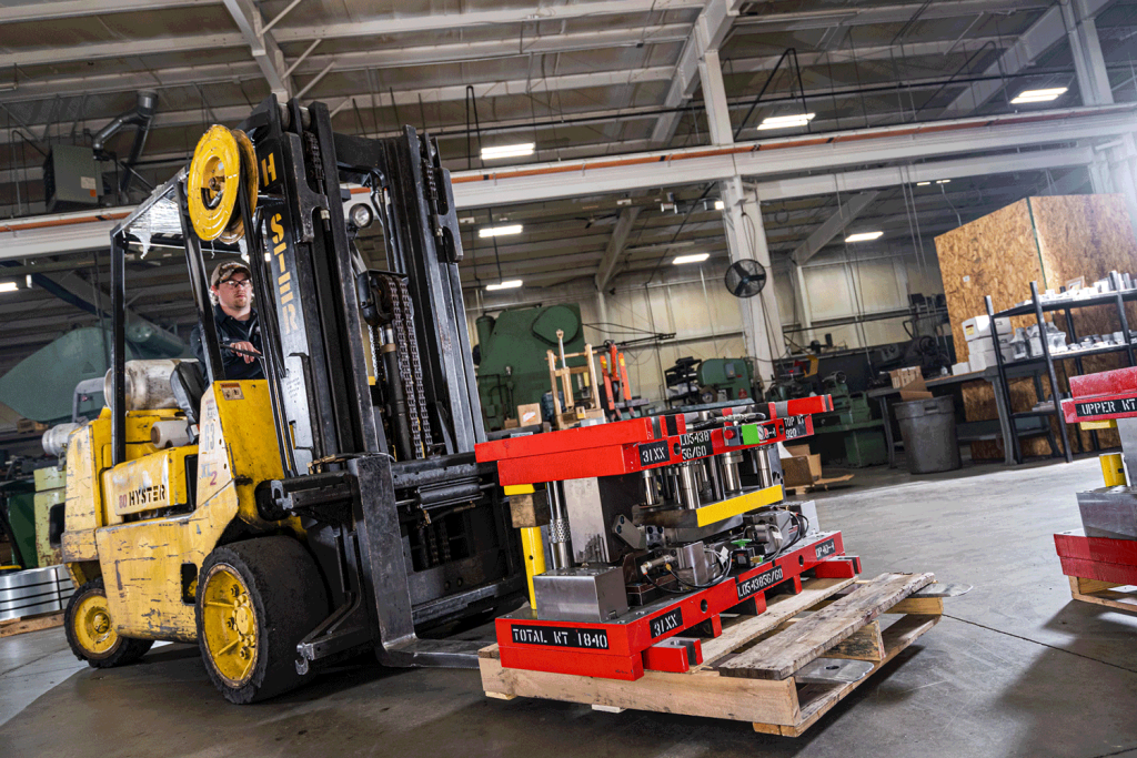 A man driving a yellow forklift through a warehouse moving raw metal materials.