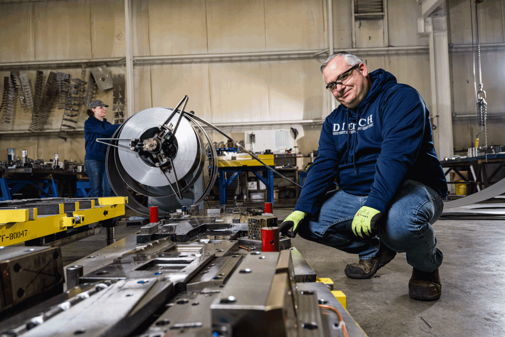 Man kneeling down by dies in industrial setting.